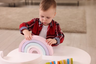 Photo of Motor skills development. Little boy playing with toys at white table indoors