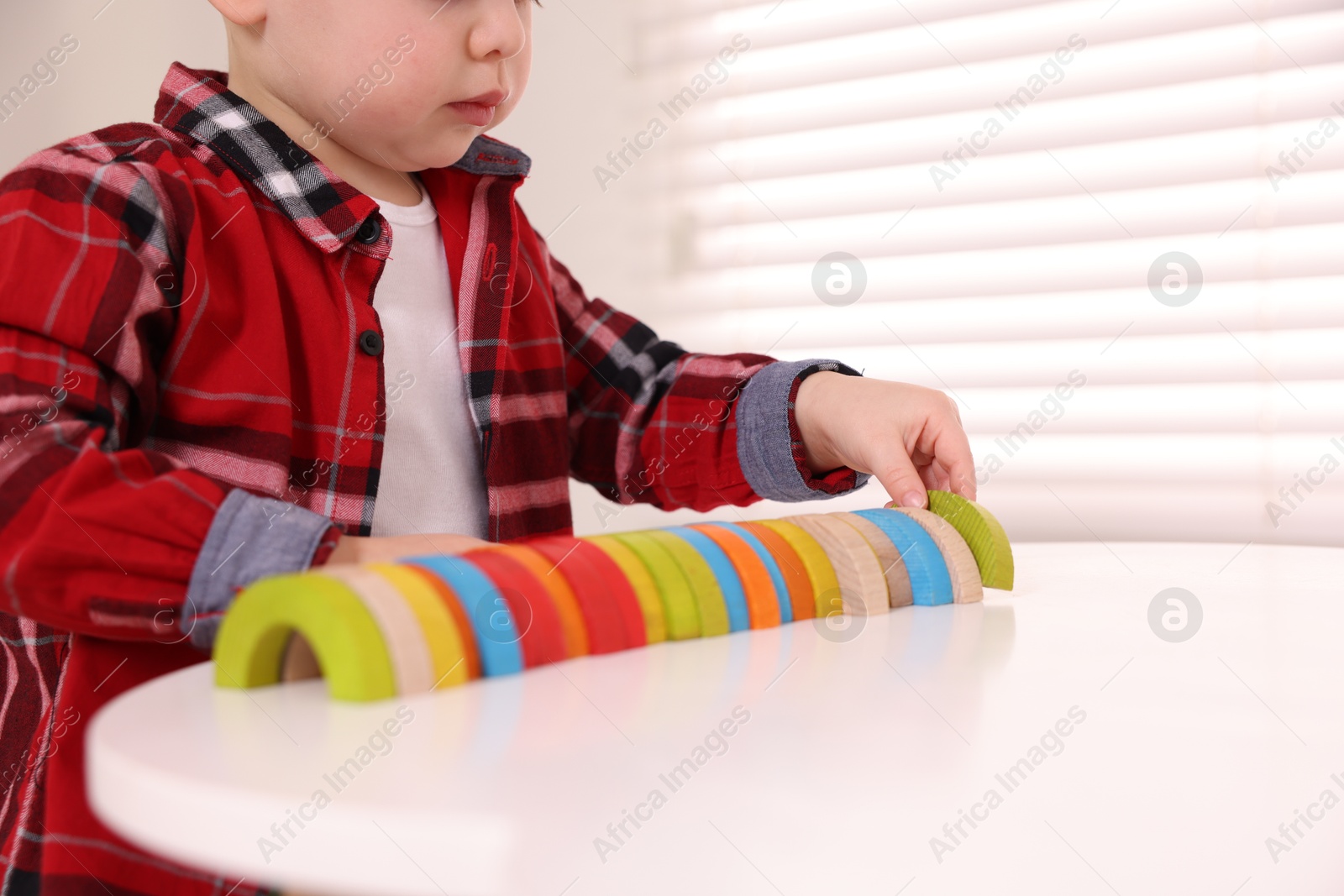 Photo of Motor skills development. Little boy playing with toys at white table indoors, closeup