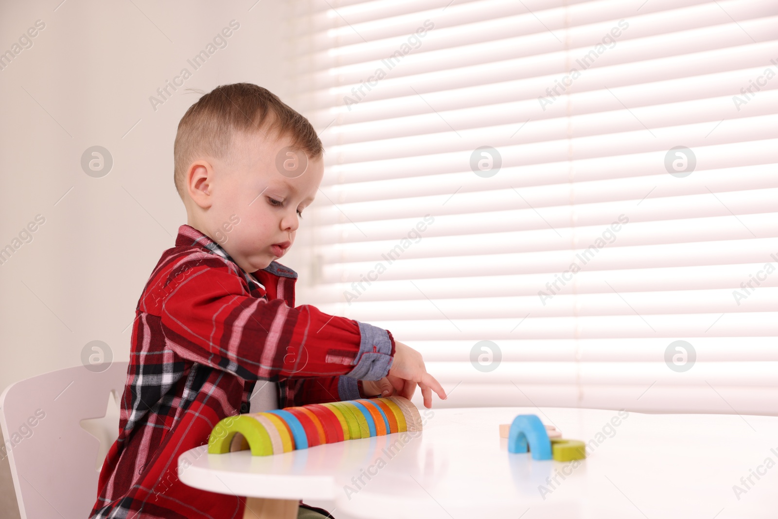 Photo of Motor skills development. Little boy playing with toys at white table indoors, space for text