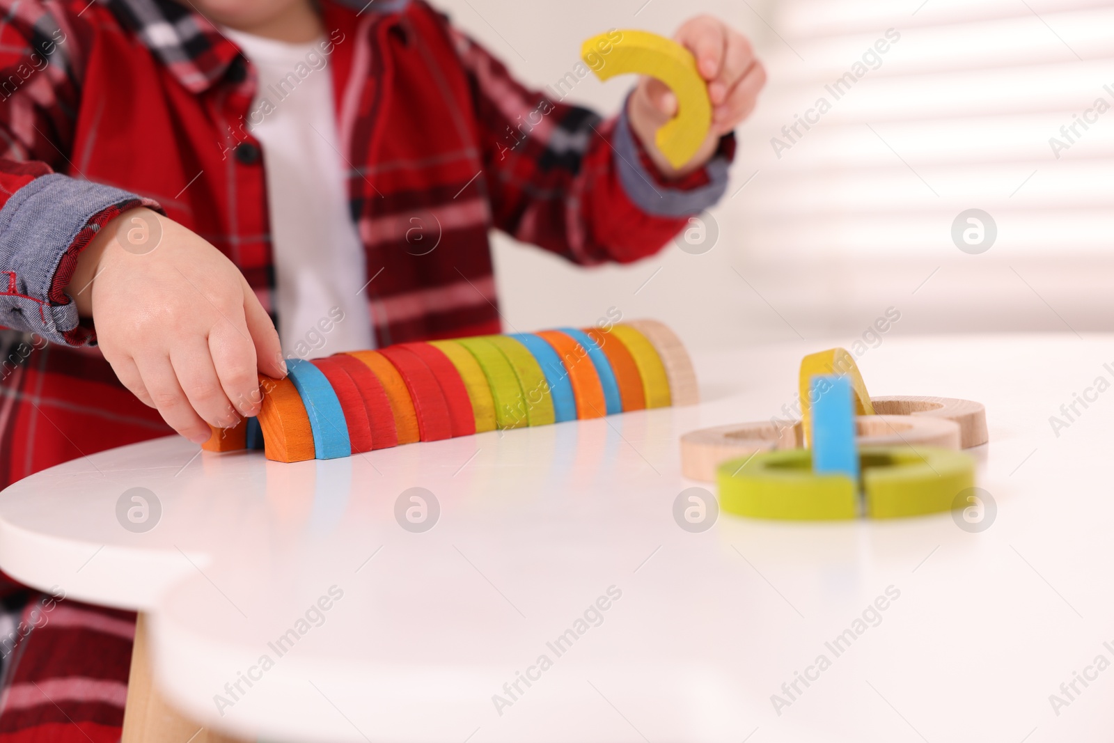 Photo of Motor skills development. Little boy playing with toys at white table indoors, closeup