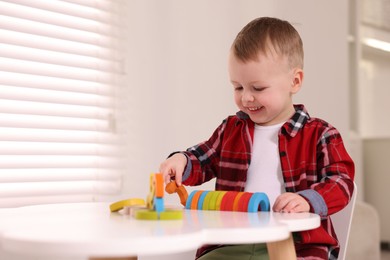 Motor skills development. Little boy playing with toys at white table indoors, space for text