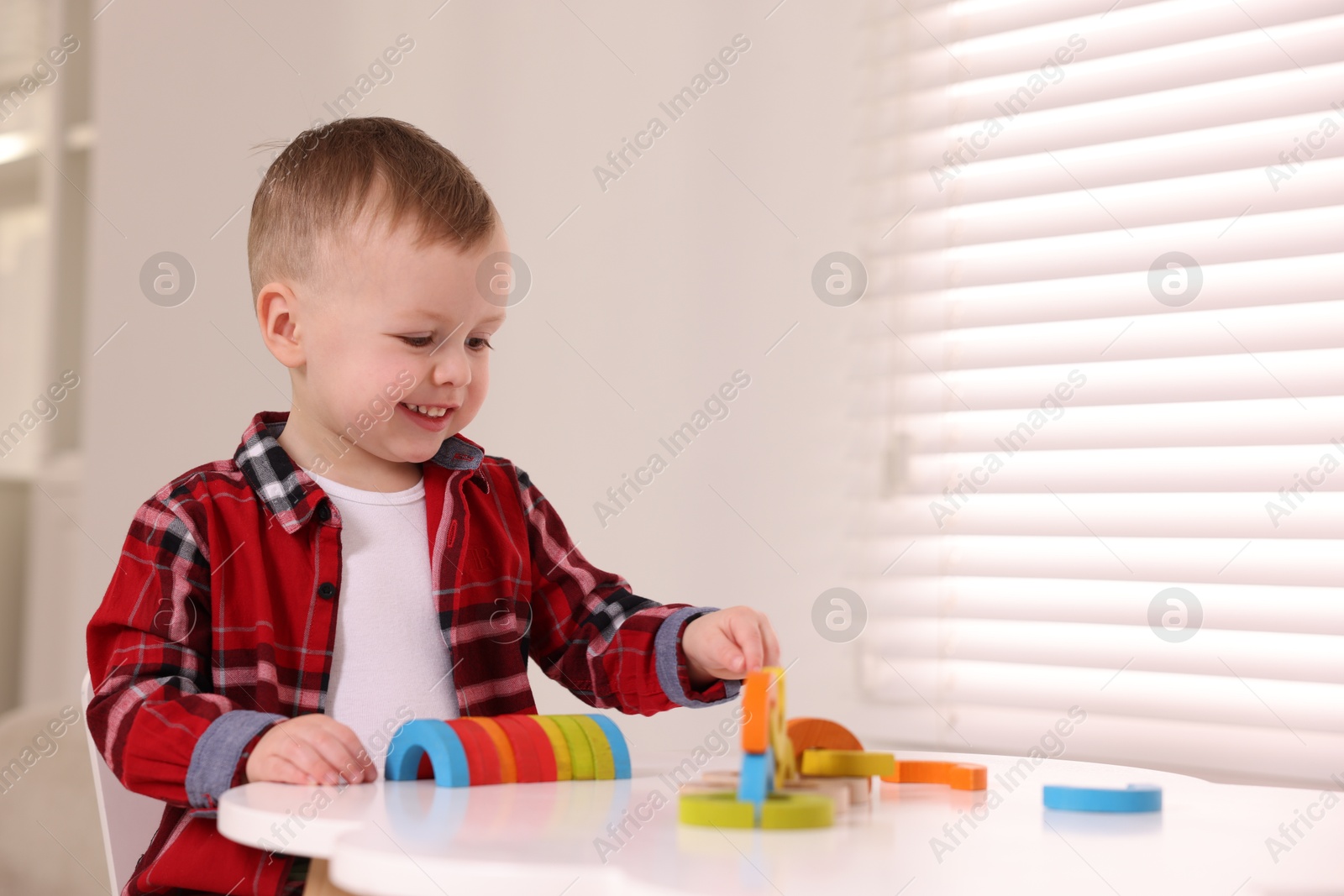 Photo of Motor skills development. Little boy playing with toys at white table indoors, space for text