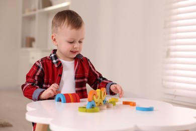 Motor skills development. Little boy playing with toys at white table indoors, space for text