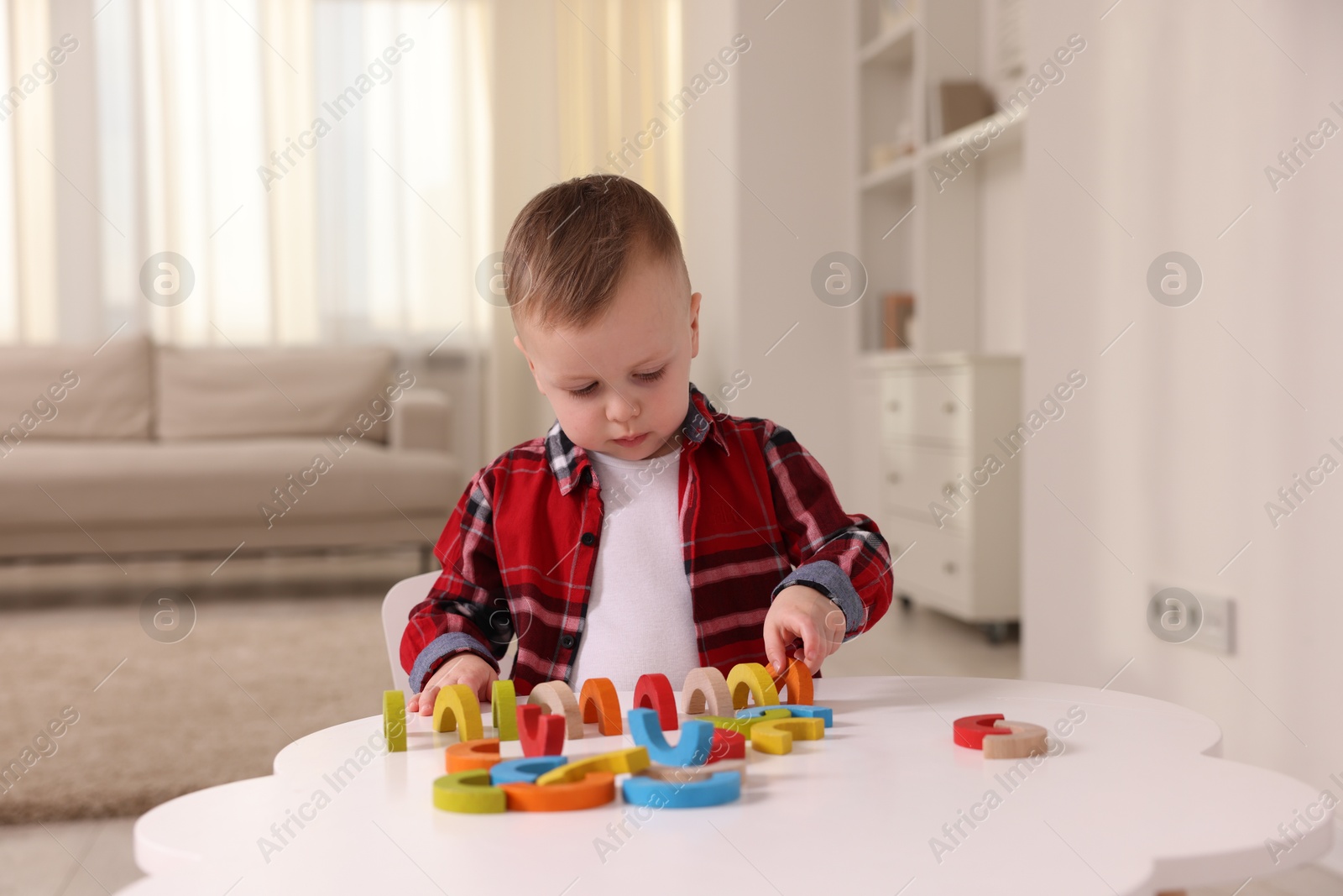 Photo of Motor skills development. Little boy playing with toys at white table indoors