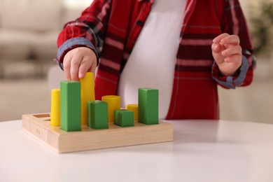 Photo of Motor skills development. Little boy playing with toys at white table indoors, closeup