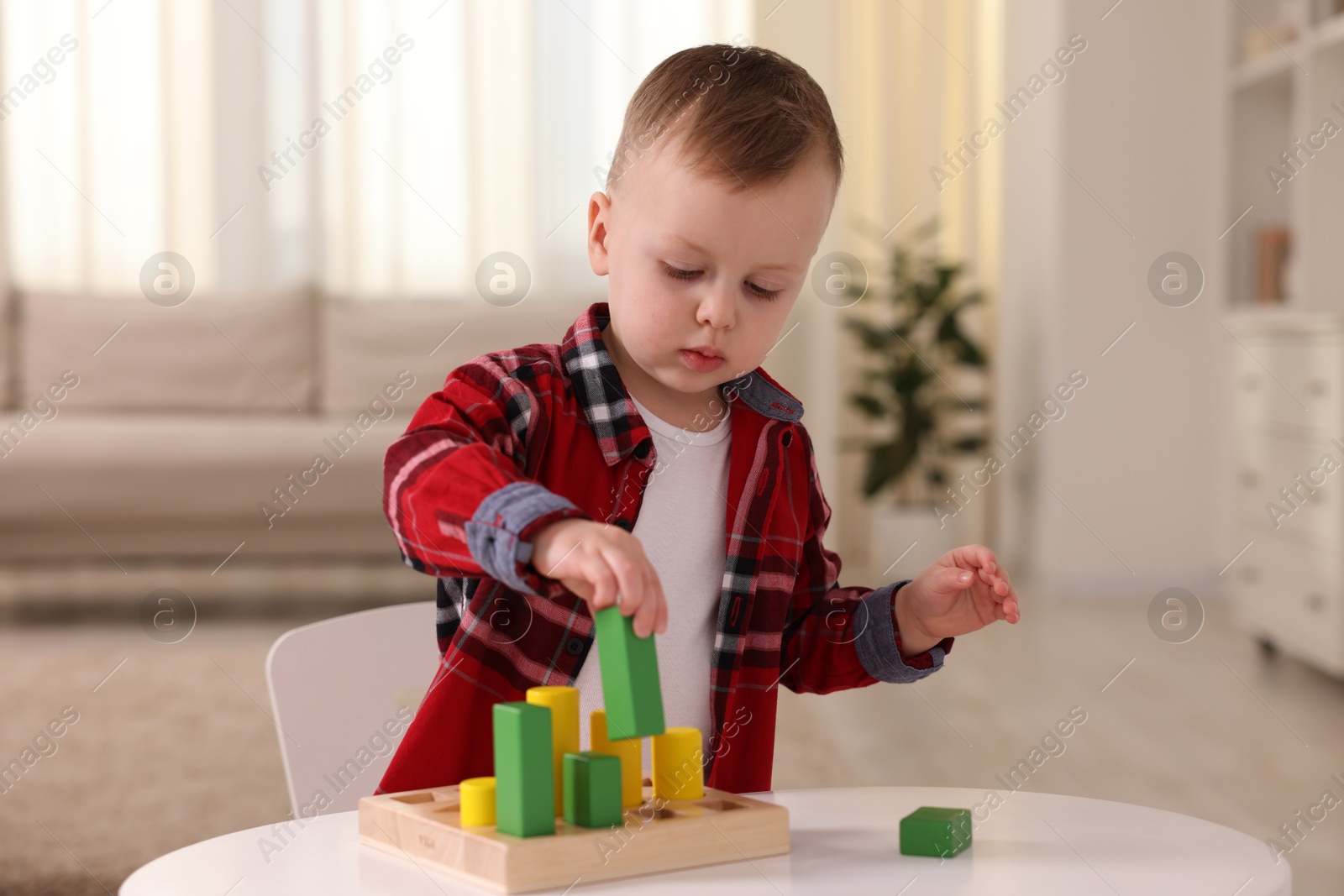 Photo of Motor skills development. Little boy playing with toys at white table indoors