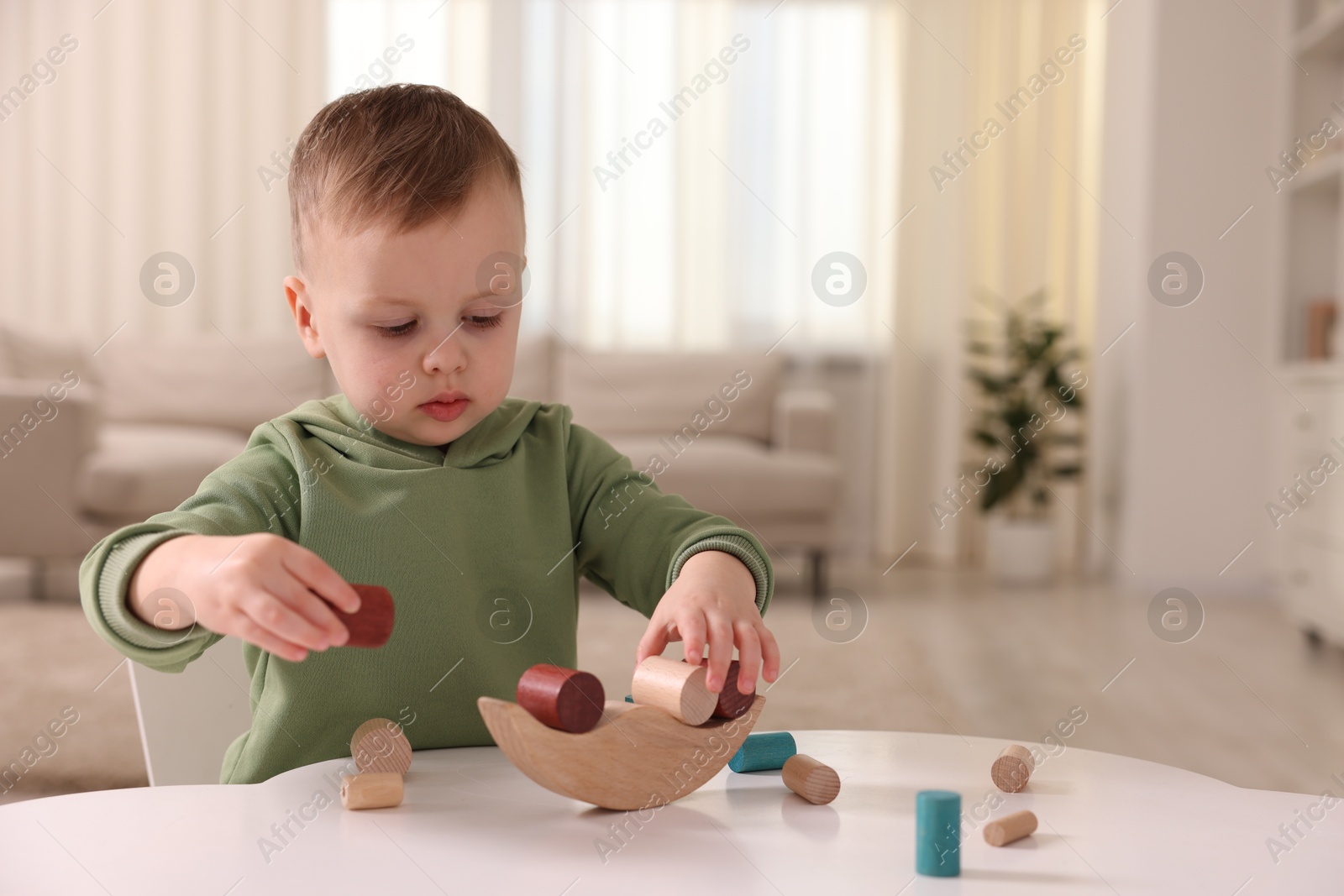 Photo of Motor skills development. Little boy playing with balance toy at white table indoors