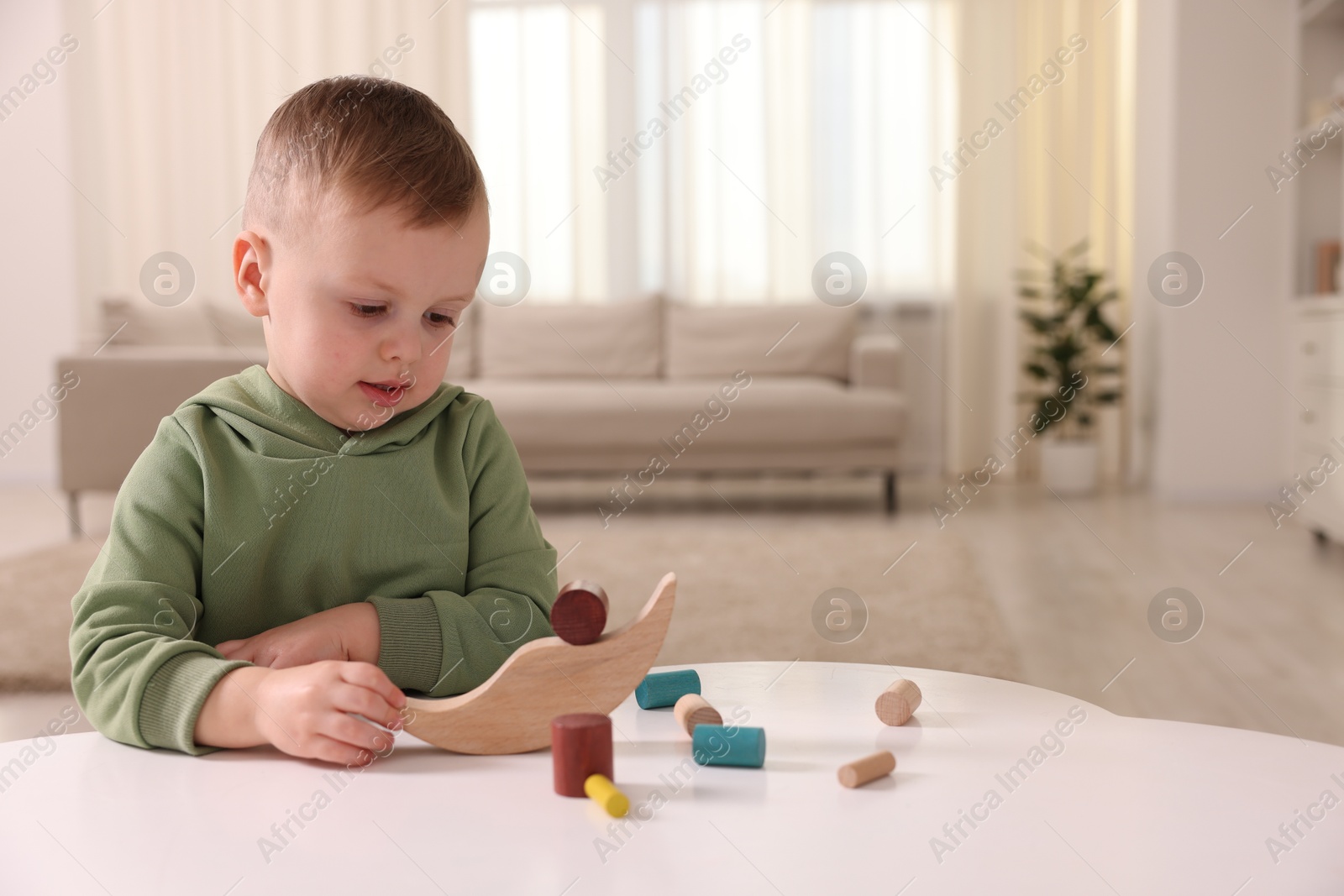 Photo of Motor skills development. Little boy playing with balance toy at white table indoors