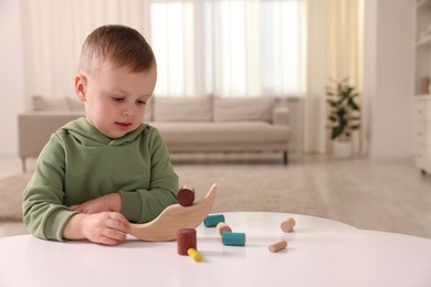 Photo of Motor skills development. Little boy playing with balance toy at white table indoors