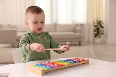 Motor skills development. Little boy playing with xylophone at white table indoors