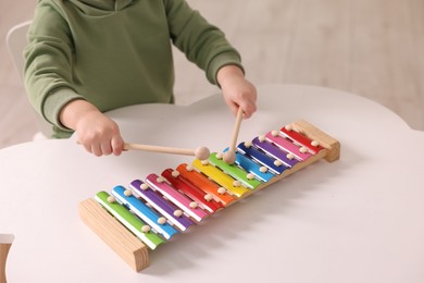 Photo of Motor skills development. Little boy playing with xylophone at white table indoors, closeup