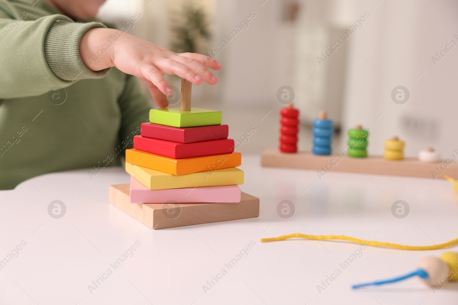 Photo of Motor skills development. Little boy playing with stacking toy at white table indoors, closeup