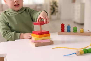 Photo of Motor skills development. Little boy playing with stacking toy at white table indoors, closeup