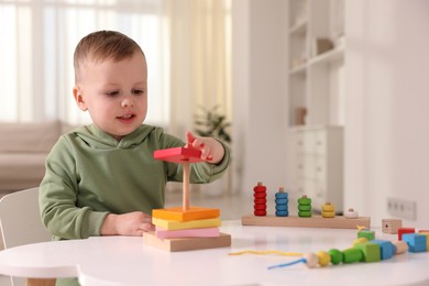 Photo of Motor skills development. Little boy playing with stacking toy at white table indoors