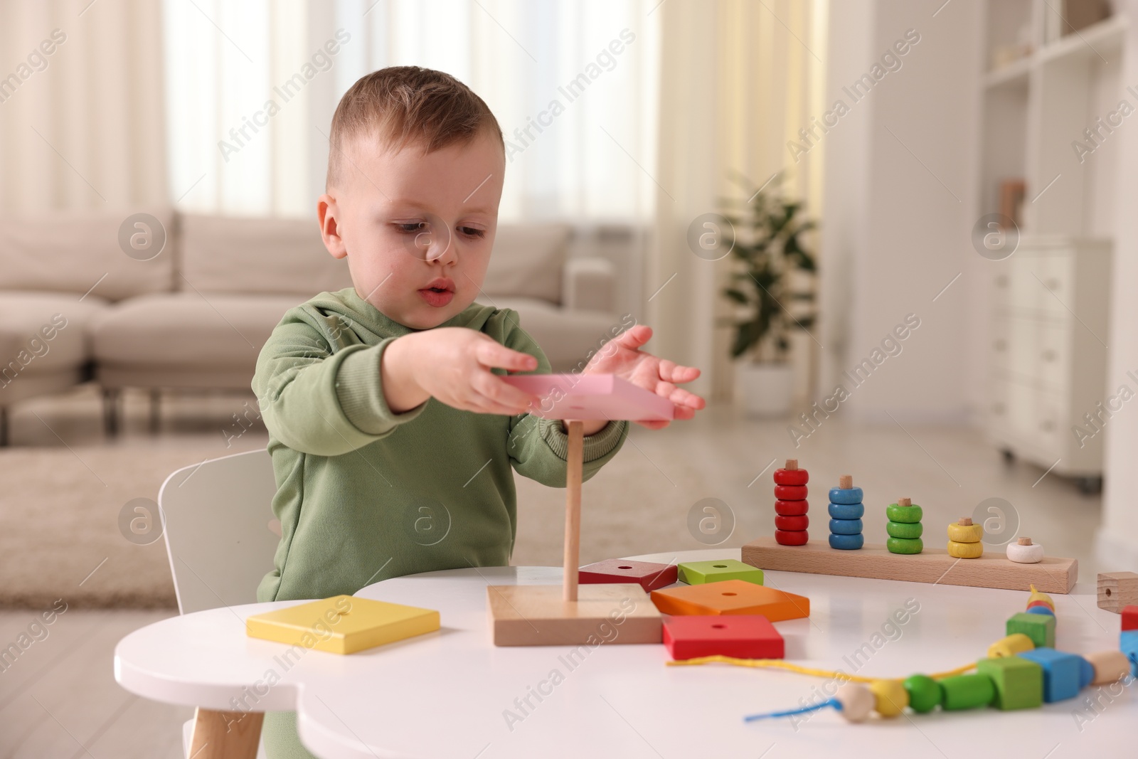 Photo of Motor skills development. Little boy playing with stacking toy at white table indoors