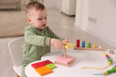 Photo of Motor skills development. Little boy playing with stacking toy at white table indoors