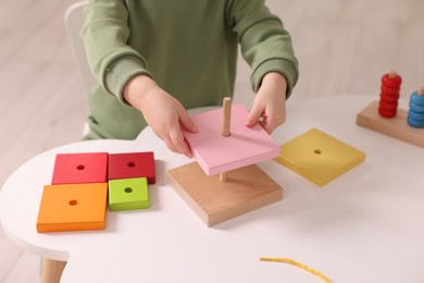 Motor skills development. Little boy playing with stacking toy at white table indoors, closeup