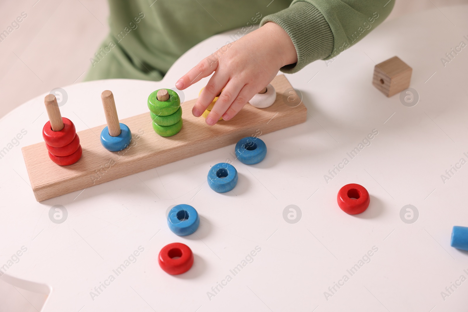 Photo of Motor skills development. Little boy playing with stacking toy at white table indoors, closeup