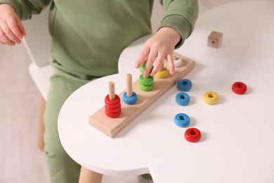 Motor skills development. Little boy playing with stacking toy at white table indoors, closeup