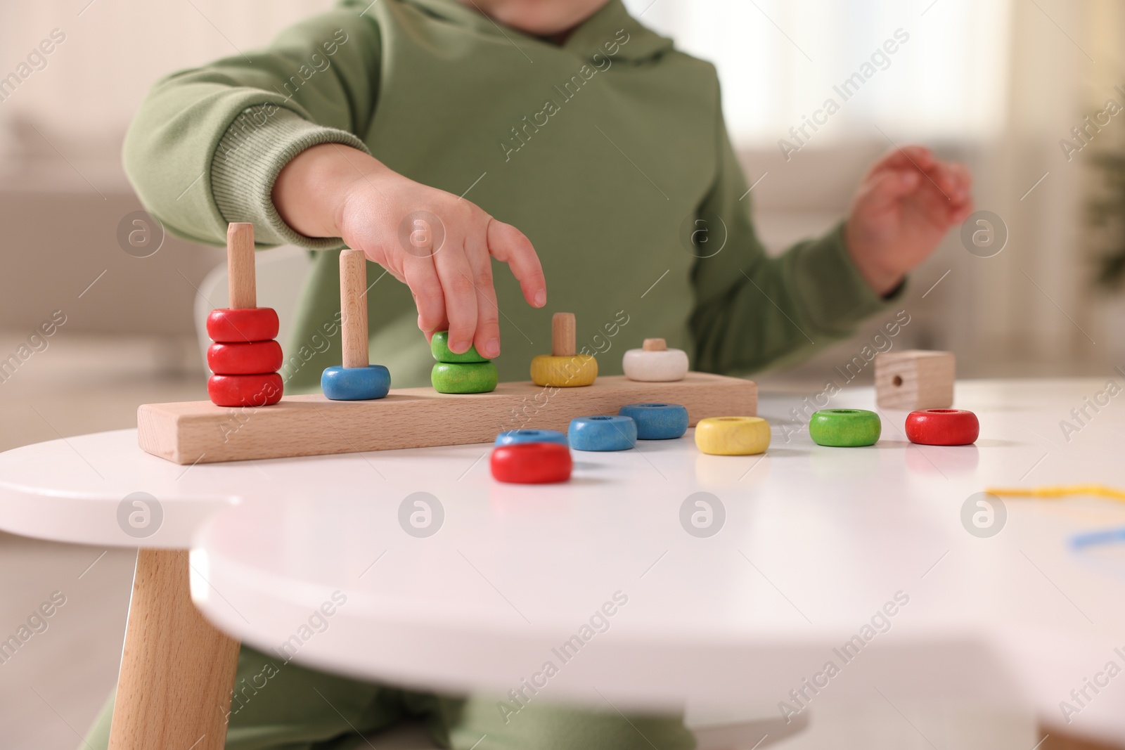 Photo of Motor skills development. Little boy playing with stacking toy at white table indoors, closeup