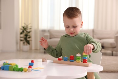 Photo of Motor skills development. Little boy playing with stacking toy at white table indoors. Space for text