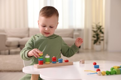 Photo of Motor skills development. Little boy playing with stacking toy at white table indoors. Space for text