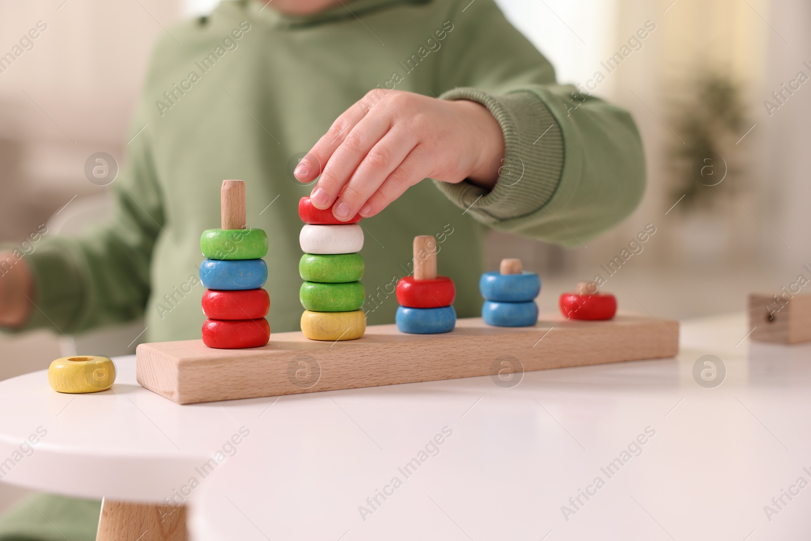 Photo of Motor skills development. Little boy playing with stacking toy at white table indoors, closeup