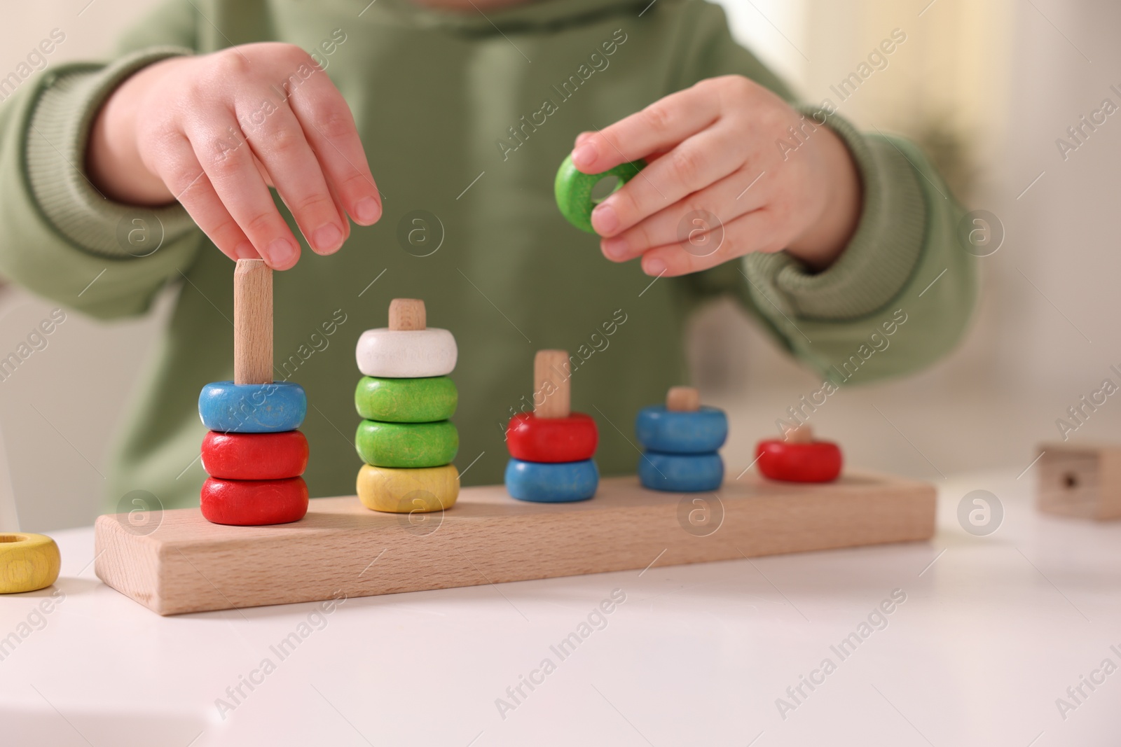 Photo of Motor skills development. Little boy playing with stacking toy at white table indoors, closeup