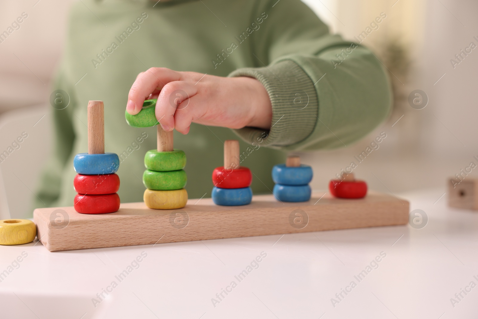 Photo of Motor skills development. Little boy playing with stacking toy at white table indoors, closeup