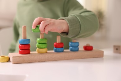 Motor skills development. Little boy playing with stacking toy at white table indoors, closeup