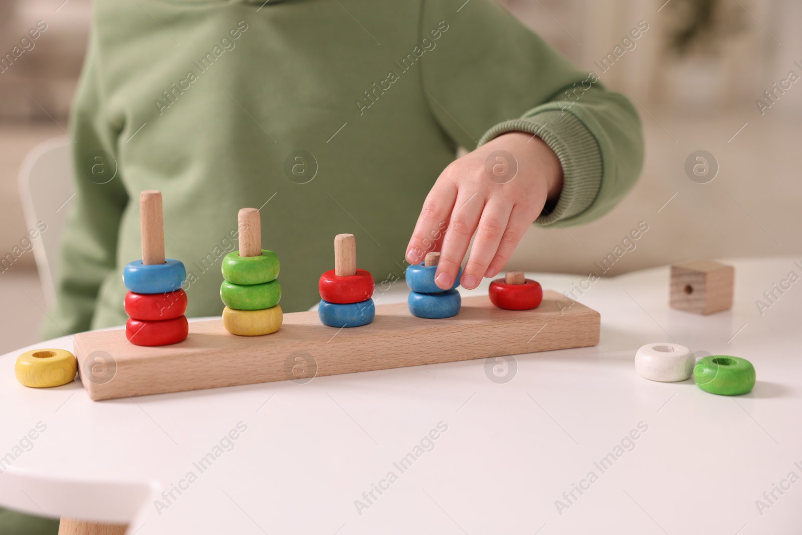 Photo of Motor skills development. Little boy playing with stacking toy at white table indoors, closeup