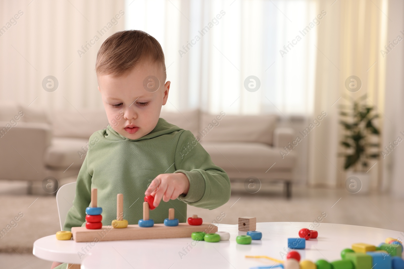 Photo of Motor skills development. Little boy playing with stacking toy at white table indoors, space for text