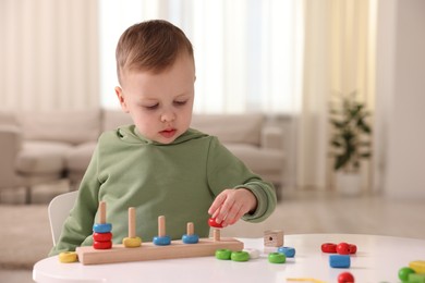 Photo of Motor skills development. Little boy playing with stacking toy at white table indoors, space for text