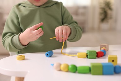 Motor skills development. Little boy playing with threading toy at white table indoors, closeup