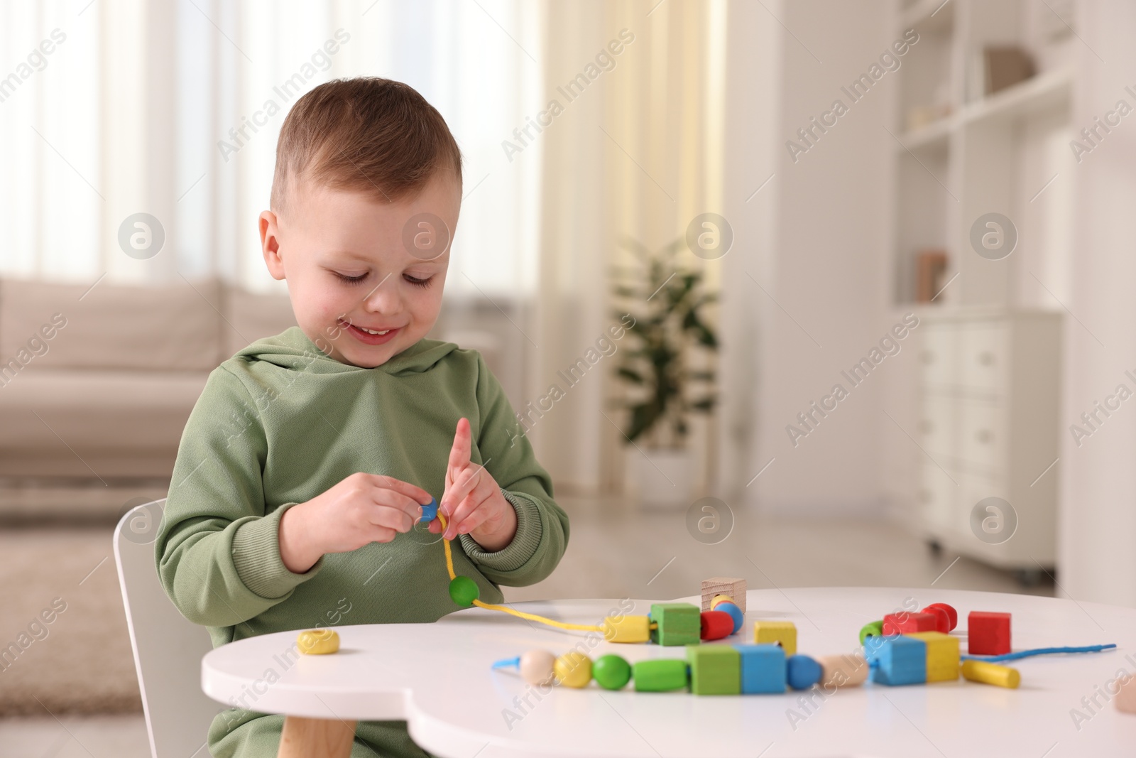 Photo of Motor skills development. Little boy playing with threading toy at white table indoors