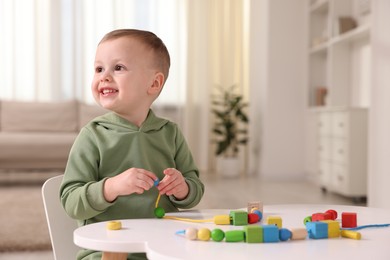 Motor skills development. Little boy playing with threading toy at white table indoors