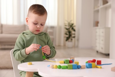 Motor skills development. Little boy playing with threading toy at white table indoors