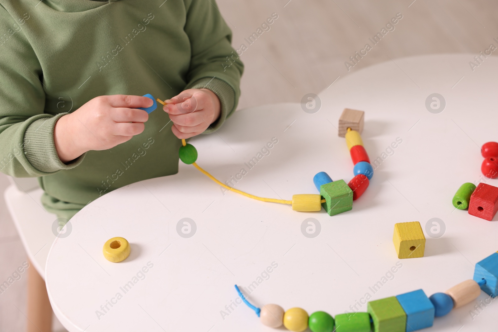 Photo of Motor skills development. Little boy playing with threading toy at white table indoors, closeup