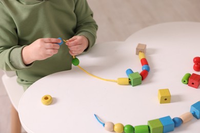 Motor skills development. Little boy playing with threading toy at white table indoors, closeup