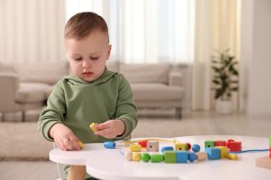 Photo of Motor skills development. Little boy playing with threading toy at white table indoors