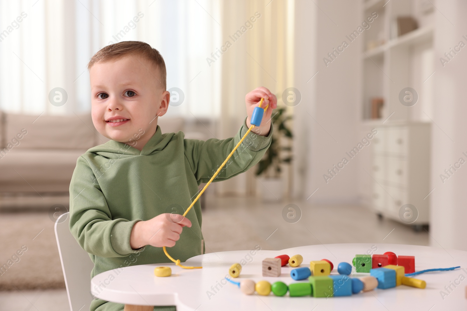 Photo of Motor skills development. Little boy playing with threading toy at white table indoors