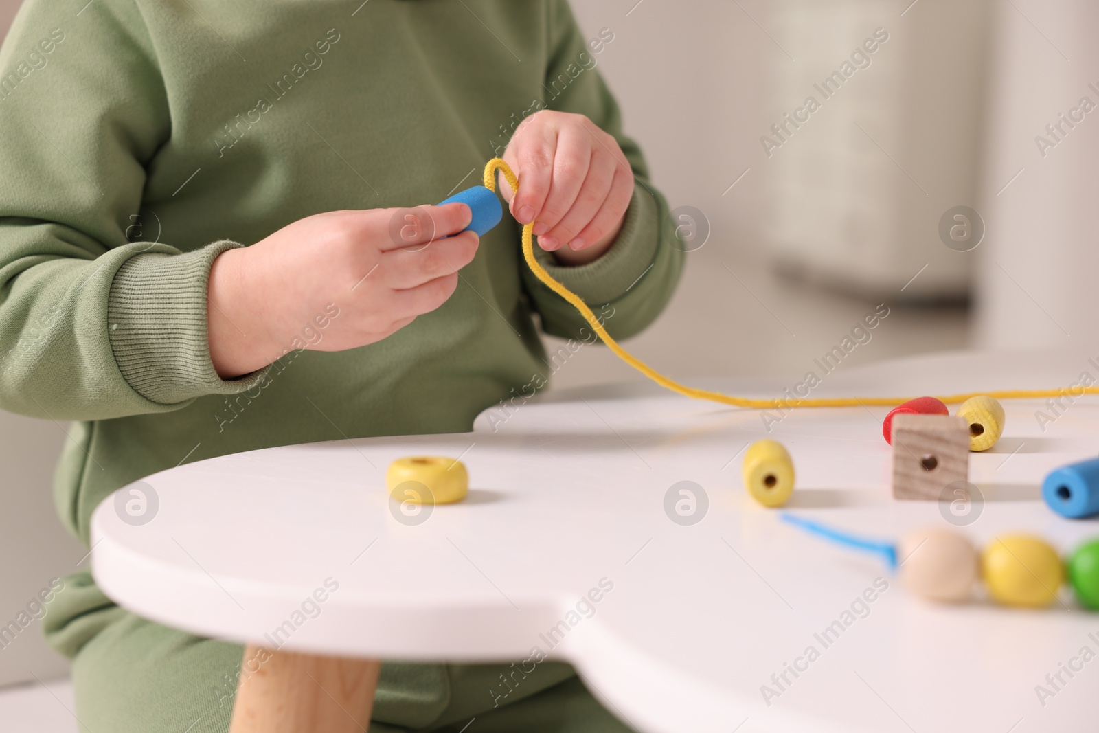 Photo of Motor skills development. Little boy playing with threading toy at white table indoors, closeup