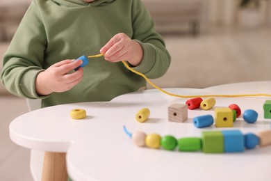 Photo of Motor skills development. Little boy playing with threading toy at white table indoors, closeup