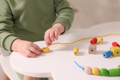 Photo of Motor skills development. Little boy playing with threading toy at white table indoors, closeup