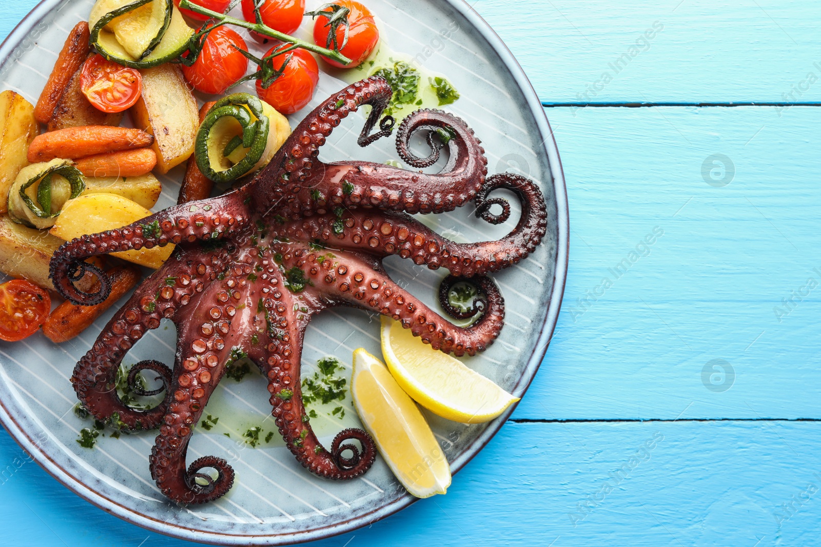 Photo of Fried octopus with herb sauce, lemon and vegetables on light blue wooden table, top view. Space for text