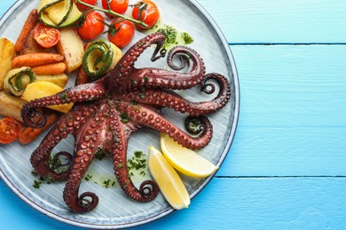 Photo of Fried octopus with herb sauce, lemon and vegetables on light blue wooden table, top view. Space for text