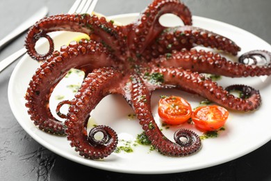 Photo of Fried octopus with herb sauce and tomatoes on dark textured table, closeup