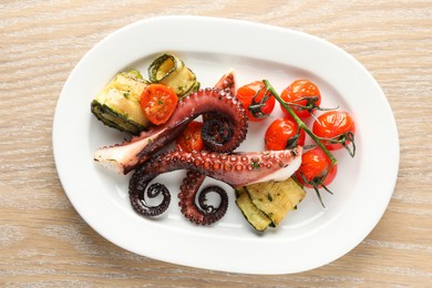 Photo of Fried octopus with zucchini and tomatoes on wooden table, top view