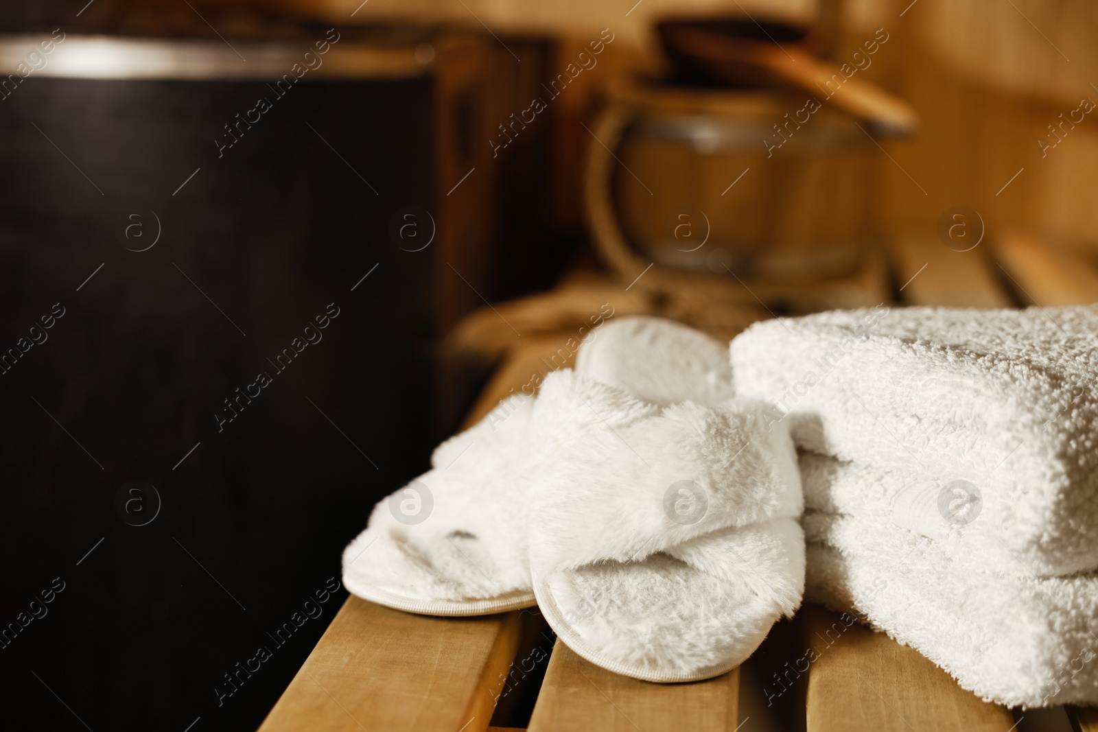 Photo of Towels and slippers on wooden bench in sauna