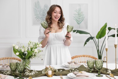 Happy young woman setting table for dinner at home